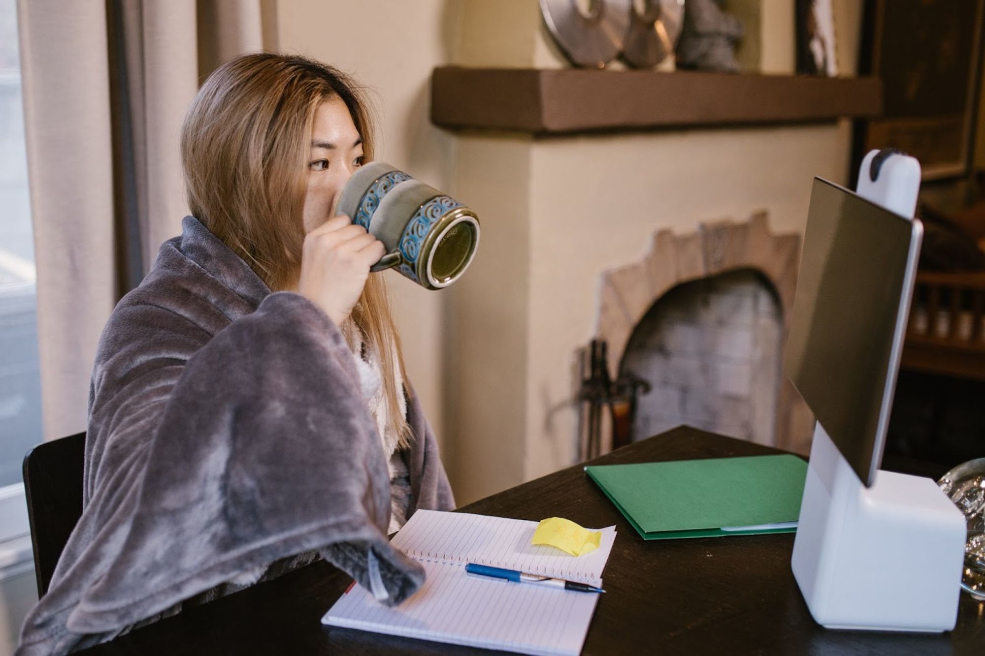 Femme emmitoufflée dans un plaid buvant un café devant son ordinateur